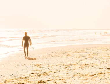 Charleston, Amerika Birleşik Devletleri - Kasım 5 2022: Genç sörfçü ellerinde dalgıç kıyafetiyle sahilde yürüyor