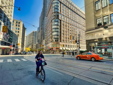 Toronto, Kanada - 24 Ekim 2022: Bir bisikletçi alışveriş merkezleri ve etrafındaki büyük binalarla kalabalık bir caddede ilerliyor