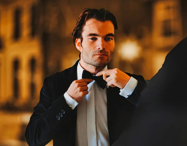 a man is preparing the bow tie of his tuxedo as preparation for an evening function