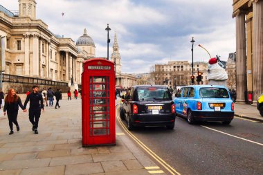 Londra, İngiltere - 6 Mart 2022: Londra 'da bir taksi geçmekte olan kırmızı bir İngiliz telefon kulübesinin önünden geçiyor ve arka planda ulusal galeri bulunuyor.