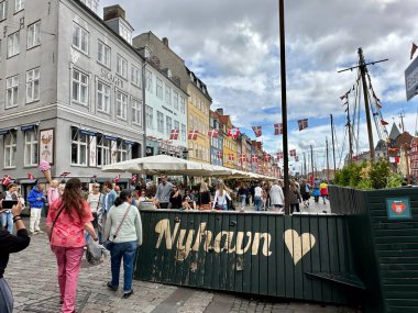 Kopenhag, Danimarka - 24 Temmuz 2023: Nemhavn 'un ünlü limanında ziyaretçiler renkli evleri ve nemhavn işaretli klasik tekneleri ile dolaşıyorlar.