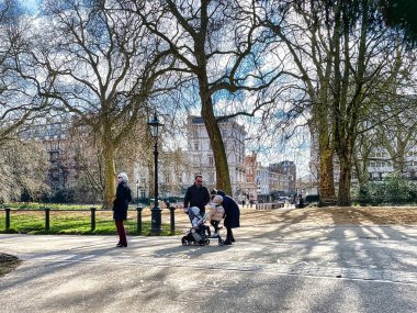Londra, Birleşik Krallık - 07 Mart 2022: İngiliz başkentindeki Hyde Park 'ta yürüyen insanlar bir bebek arabasını iterek