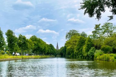 Voorburg, Hollanda - 19 Haziran 2022: canlı mavi gökyüzü boyunca tipik bir kanal boyunca zarif bir tarihi Hollanda kilise kulesi