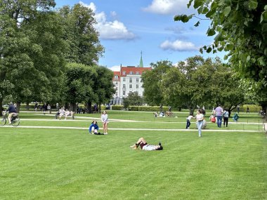 Kopenhag, Danimarka - 25 Temmuz 2023: ünlü Rosenborg şatosu etrafını çevreleyen güzel yeşil parkla birlikte insanlar eski kasabanın yakınında eğleniyor.