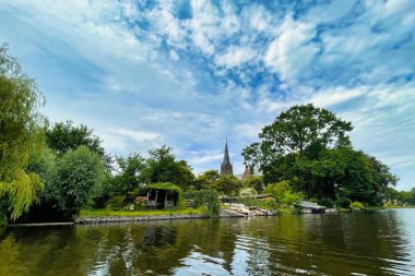 Voorburg, Hollanda - 19 Haziran 2022: canlı mavi gökyüzü boyunca tipik bir kanal boyunca zarif bir tarihi Hollanda kilise kulesi