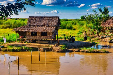 Bago, Myanmar - 02 Aralık 2012: Geleneksel Myanmar bambu kırsal evi ya da kırsal kesimde nehir ve uzun kuyruklu teknelerin bulunduğu cambaz ayaklıkları üzerindeki kulübe