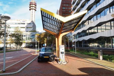 Den Haag, Hollanda - 03 Kasım 2021: bir elektrikli araba park halinde ve bir şehrin ofis bölgesinde bir kamu şarj istasyonunda şarj ediliyor