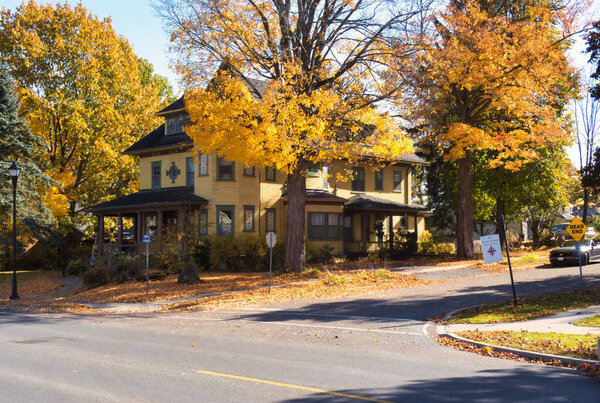 gananoque, canada - 22 October 2022 : residential neighborhood street with historic house and trees in vibrant fall orange