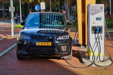 Den Haag, Hollanda - 03 Kasım 2021: bir elektrikli araba park halinde ve bir şehrin ofis bölgesinde bir kamu şarj istasyonunda şarj ediliyor
