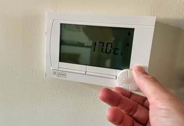 Den Haag, Hollanda - Kasım 04 2021: Bir kişinin eli bir termostatın sıcaklığını düşürür