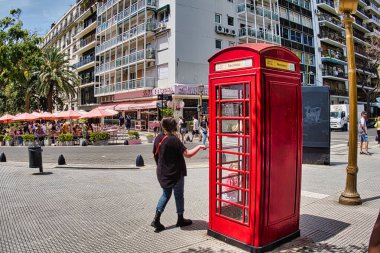 buenos aires, argentina - 28 October 2022: a woman is walking on the square next to the Recoleta cemetery and passes a typical red british phone booth clipart