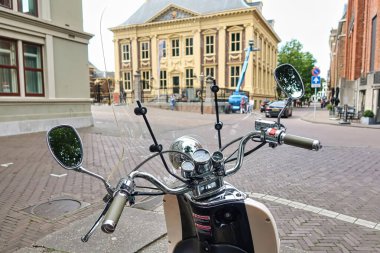 Lahey, Hollanda - 20 Ağustos 2021: Arkaplanda Mauritshuis ile birlikte tarihi şehrin merkezine parlak krom klasik bir scooter park edilmiştir.