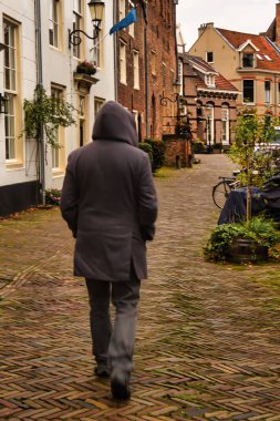 Amersfoort, Hollanda - 25 Ekim 2020: Gri ceketli kapüşonlu bir adam tarihi bir Hollanda şehrinin caddesinde yürüyor.