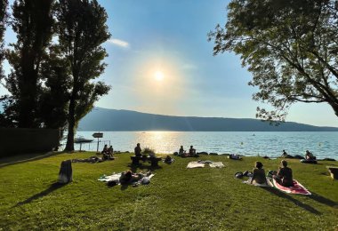 Menthon Aziz Bernard, Fransa - 08 Eylül 2021: Ek bina gölü boyunca çimlerin üzerinde uzanan insanları siluet içinde güneşlendirme