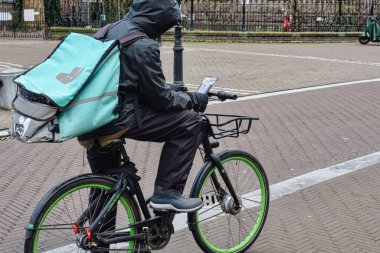 The Hague, Netherlands - January 03 2022: a food delivery person is standing on his bicycle checking the screen of his mobile phone for instructions