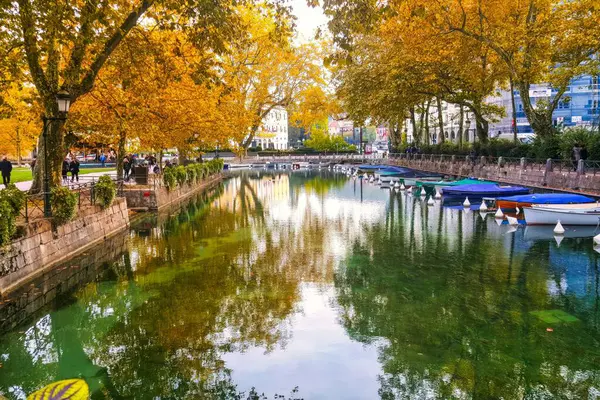 stock image Annecy, France - Augustus 20, 2008: Old harbor canal with big trees hanging over the water making a romantic atmosphere. Bridge of the lovers in the background and small boats