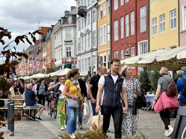Kopenhag, Danimarka - 24 Temmuz 2023: Ziyaretçiler renkli evleri ve klasik tekneleriyle nyhavn ünlü limanında yürüyorlar