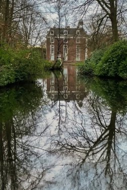 Den Haag, Hollanda - 20 Aralık 2021: Ormandaki küçük Alman şatosu ağaçlarla çevrilidir ve su yüzeyinde bir yansıma görülebilir.