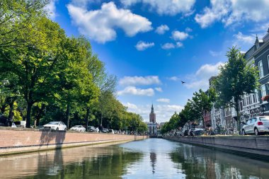 Lahey, Hollanda - 19 Haziran 2022: canlı mavi gökyüzü boyunca tipik bir kanal boyunca zarif bir tarihi Hollanda kilise kulesi