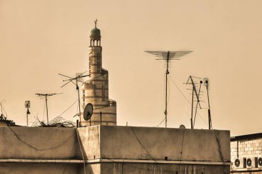 Doha, Qatar - January 26 2010 : a minaret over of the big mosque build from white clay is seen from all directions over the roofs clipart