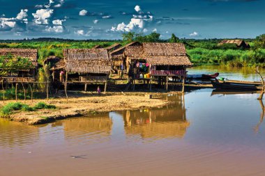 Bago, Myanmar - 02 Aralık 2012: Geleneksel Myanmar bambu kırsal evi ya da kırsal kesimde nehir ve uzun kuyruklu teknelerin bulunduğu cambaz ayaklıkları üzerindeki kulübe