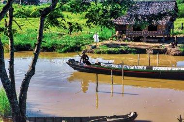 Bago, Myanmar - 02 Aralık 2012: Geleneksel Myanmar bambu kırsal evi ya da kırsal kesimde nehir ve uzun kuyruklu teknelerin bulunduğu cambaz ayaklıkları üzerindeki kulübe