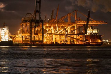 Rotterdam, Hollanda - 22 Kasım 2021: Deniz konteynırları geceleri aydınlanan dev vinçler tarafından gemilerden indiriliyor