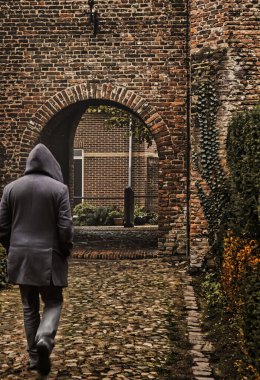 Amersfoort, Hollanda - 25 Ekim 2020: Kapüşonlu bir adam akşamleyin tarihi bir ortaçağ Hollanda şehrinin kapısına doğru yürüyor.