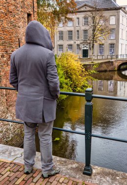 Amersfoort, Hollanda - 25 Ekim 2020: gri Voat kapüşonlu bir adam eski bir Hollanda kasabasında eski bir tuğla köprü parçası üzerinde duruyor