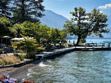 talloires, france - June 25 2023: prepared terrace tables and umbrellas of a restaurant laying at the edge of the annecy mountain lake clipart