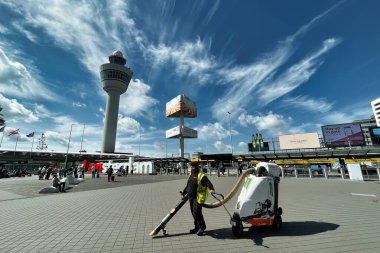 schiphol, Hollanda - 12 Haziran 2022: Havaalanı terminallerinin dışında yürüyen yolcular bir trafik işareti, bir kontrol kulesi ve reklam panoları ile