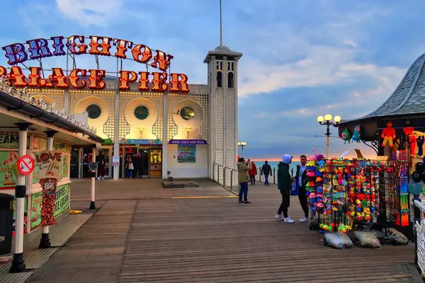 Brighton, İngiltere - Mart 04 2022: İngiliz sahil beldesinin tarihi rıhtımında neon ışıkları, atari oyunları ve sıcak günbatımı renkleriyle yürüyen insanlar
