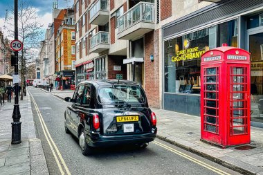Londra, İngiltere - 7 Mart 2022: Londra 'da bir taksi kırmızı bir İngiliz telefon kulübesinin önünden geçiyor.