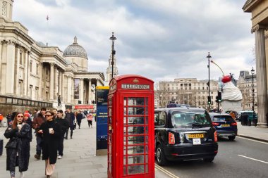Londra, İngiltere - 6 Mart 2022: Londra 'da bir taksi geçmekte olan kırmızı bir İngiliz telefon kulübesinin önünden geçiyor ve arka planda ulusal galeri bulunuyor.