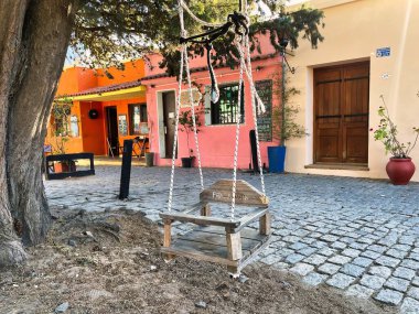 colonia del sacramento, uruguay - november 1 2022: a swing is hanging on a tree on the cobble stone streets in the old barrio historico of this unesco world heritage site clipart