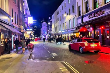 London, United Kingdom - March 6 2022: a vibrant Soho street with clubs nightlife restaurant and bars with many hip young people and vibrant colored illumination