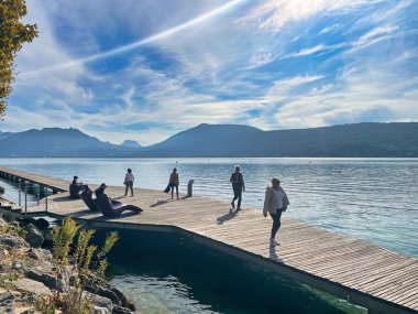 Annecy, Fransa - 15 Ekim 2021: İnsanlar bir dağ gölünün rıhtımında rahatça yürüyüp güneşin ve manzaranın tadını çıkarıyorlar.