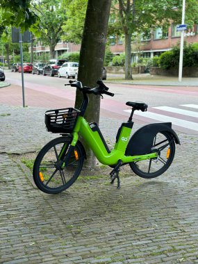 Hollanda, den haag - 23 Mayıs 2024: Elektrikli bisiklet ya da bisiklet paylaşım sistemi adı verilen caddeye park edilmiş bir ağacın yanına git