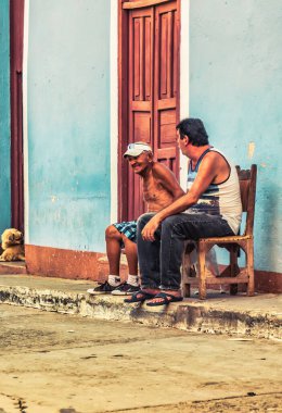 Trinidad, Cuba - July 15 2018 :A former spanish colonial town still in the 18th century. Old men sitting on chairs outside on the side walk talking. clipart