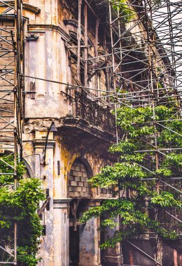 Havana, Cuba - July 06 2018 : AS there is no money to take care of these colonial era buildings the scaffolding is overgrown with plants. clipart