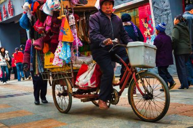 Chengdu, Çin - 29 Kasım 2009: Yaşlı bir vatandaş kaldırımda bisiklet sürerken mallarını satıyor ve taşıyor