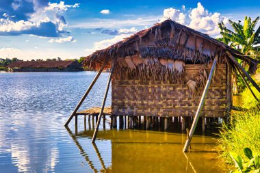 Bago, Myanmar - 02 Aralık 2012: Geleneksel Myanmar bambu kırsal evi ya da kırsal kesimde nehir ve uzun kuyruklu teknelerin bulunduğu cambaz ayaklıkları üzerindeki kulübe