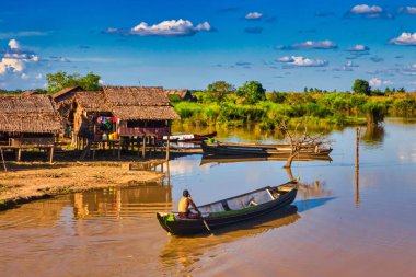 Bago, Myanmar - December 02 2012 : a traditional Myanmar bamboo rural house or hut on the countryside on stilts with river and long tailed boat clipart