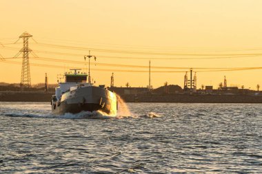 Rotterdam, Hollanda - 22 Kasım 2021: Gün batımında bir limanın yüzeyinde bir römorkör yüzüyor.