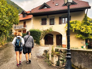 Menthon Aziz Bernard, Fransa - 10 Eylül 2021: İki yürüyüşçü veya turist tarihi evleri olan küçük bir Fransız dağlık köyünün yamaçlarında yürüyorlar