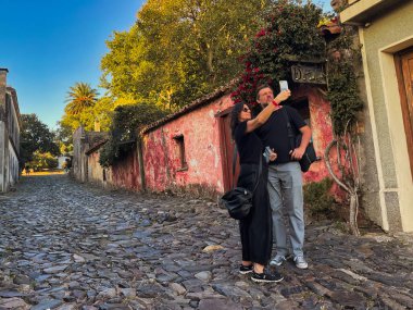 colonia del sacramento, uruguay - november 2 2022: tourists walking on cobble stone unesco world heritage site colonial street and taking picture clipart