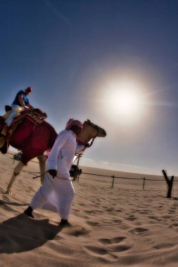 Doha, Katar - 28 Ocak 2010: Turistler başörtüsü ve buzları çözülen bir adamla çölde deve sürmek kadar eğleniyorlar.