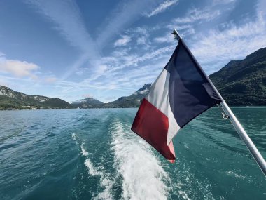 Talloires, Fransa - Eylül 06 2024: Annecy Gölü üzerinde sakin bir tekne gezisi Fransız bayrağının canlı renklerini gözler önüne seriyor. Resimli dağlar görkemli bir şekilde yükseliyor berrak bir gökyüzünün ortasında,