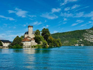 duingt, france - September 06 2024: The picturesque Chateau de Duingt stands majestically on the shores of Lake Annecy, framed by green trees against a backdrop of bright blue skies and calm waters. clipart