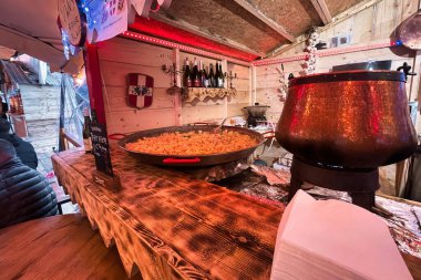 thones, france - december 31 2022: a typical pan with a giant tartiflette dish is prepared at a stall on a festival clipart